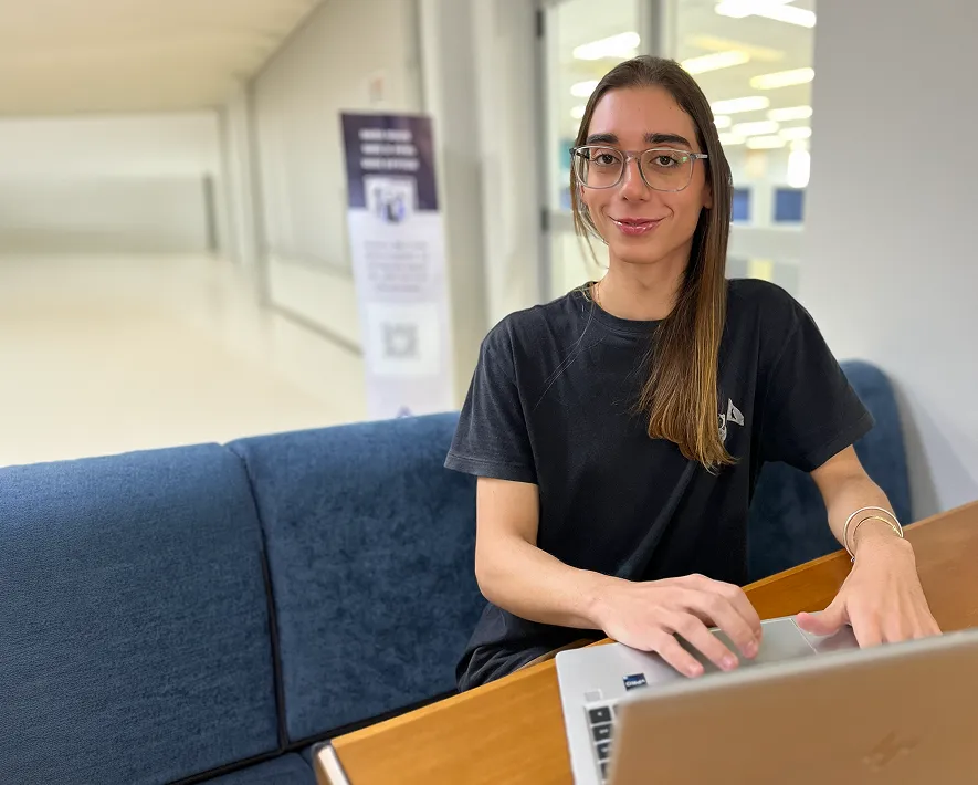 Jovem estagiária sorrindo sentanda em uma mesa no escritório