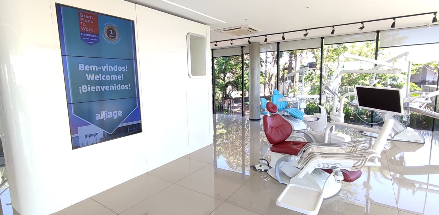 Foto com duas cadeiras de dentistas, uma com estofado vermelho e a outra com estofado azul. Ao fundo uma paisagem natural