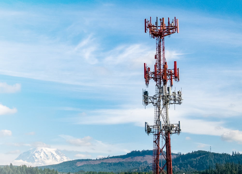 Antena de comunicação e montanhas e céu azul com nuvens ao fundo.