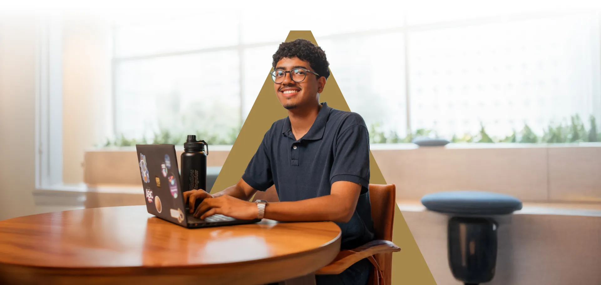 Jovem de óculos sorrindo enquanto utiliza notebook no escritório