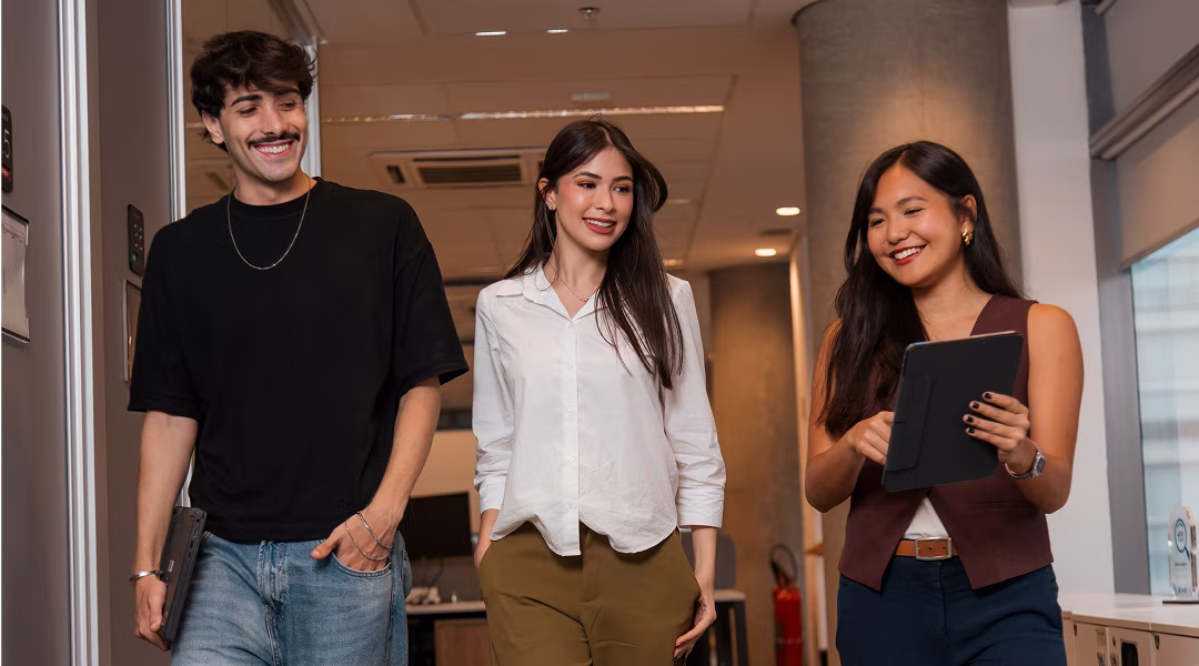 Jovens sorrindo enquanto conversando e andam pelo corredor do escritório