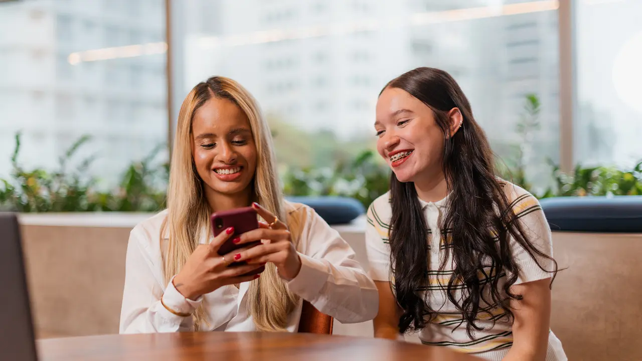 Duas estagiárias sorrindo enquanto utiliza o celular