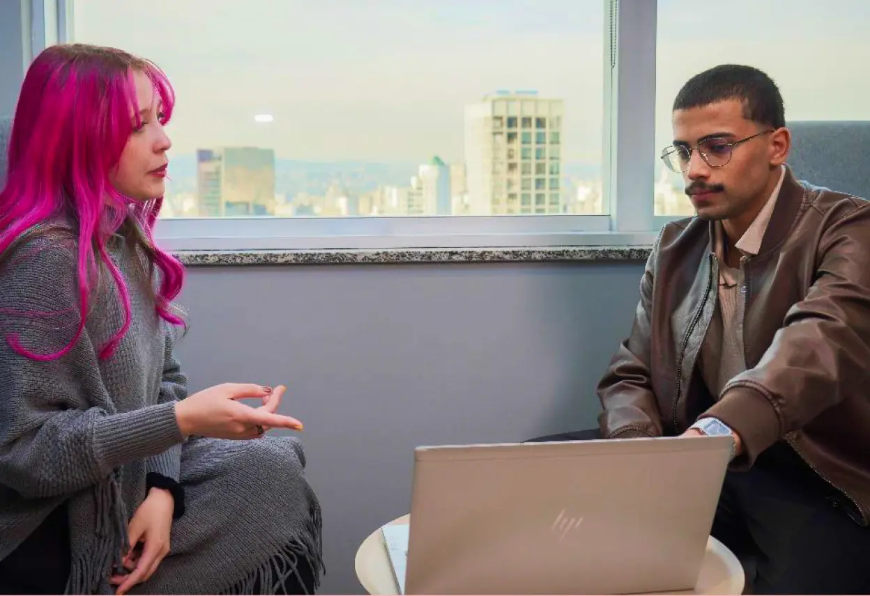 Dois jovens estagiários conversando no escritório enquanto utiliza o notebook