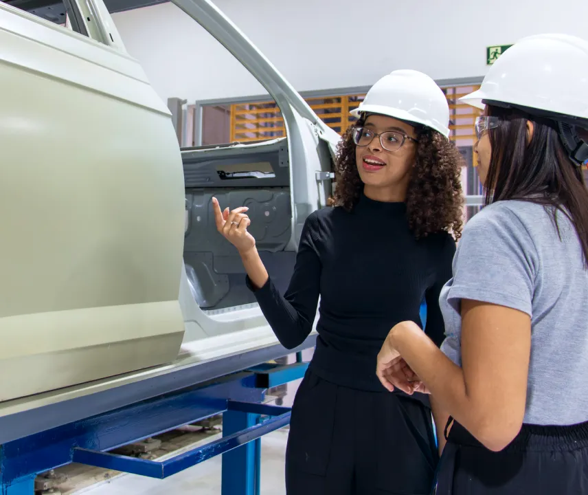 Uma estgiária explicando sobre um processo na fábrica para outra pessoa