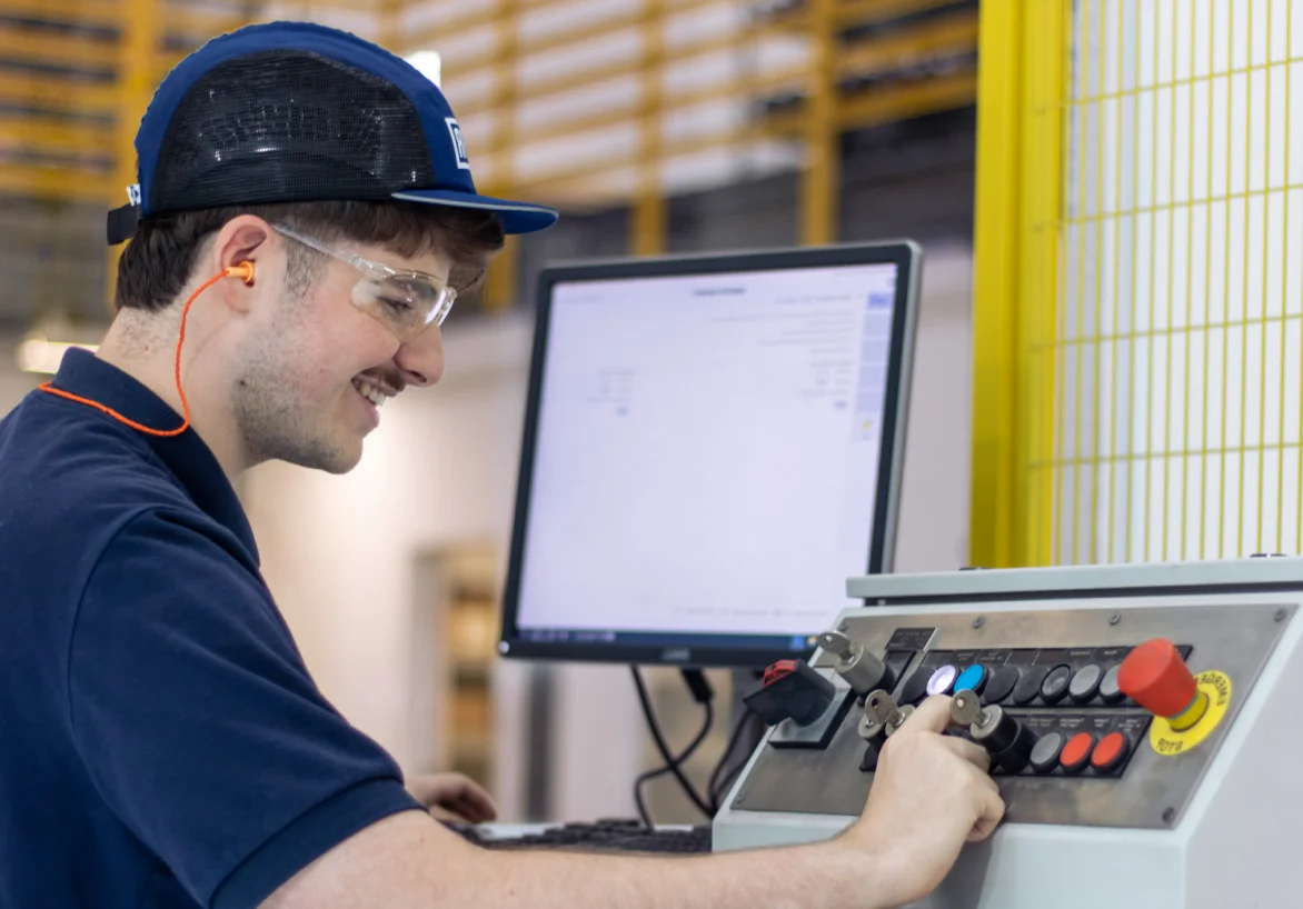 Jovem colaborador sorrindo utilizando EPI mexendo na maquina