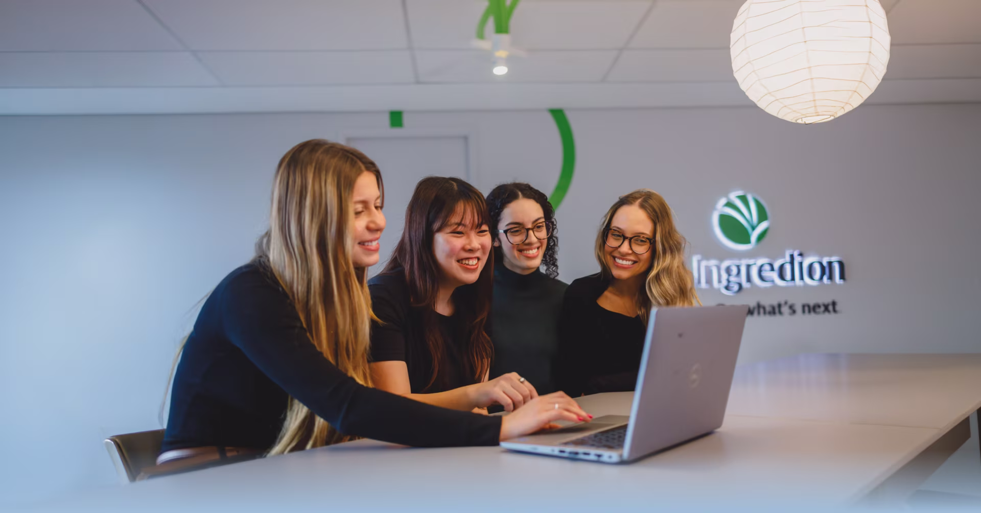 Quatro jovens reunidas em torno de um notebook no escritório da Ingredion