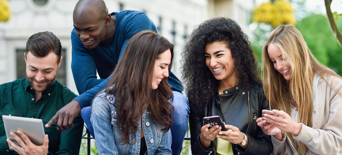 Grupo de estagiários interagindo e sorrindo com celular e tablet na mão 