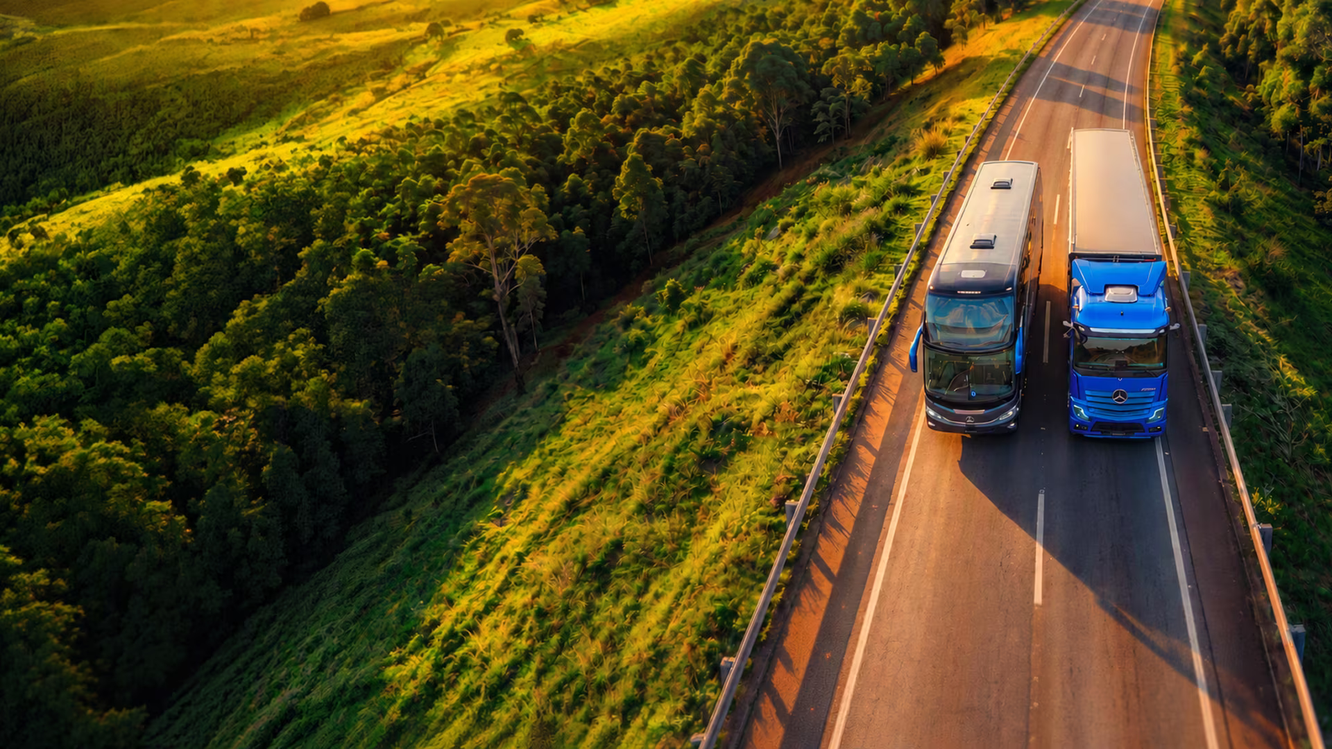 Caminhão e ônibus Mercedes-Benz trafegam lado a lado em uma rodovia cercada por vegetação