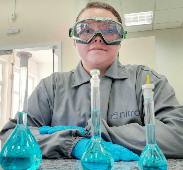 Estagiária no laboratório com produtos químicos, uniforme e epi