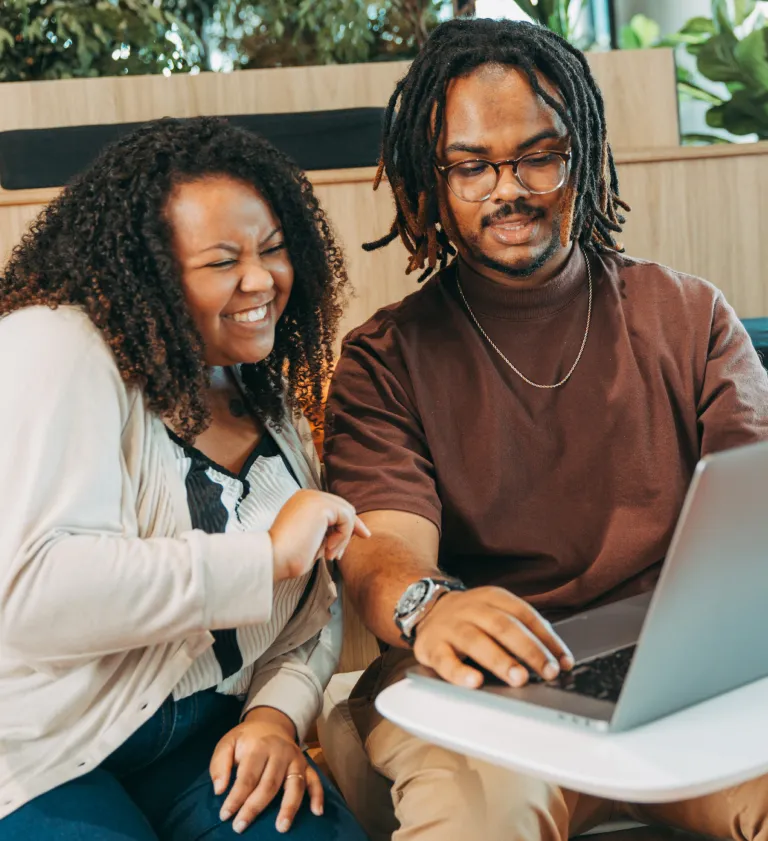 Dois jovens negros sorrindo enquanto utilizam o computador