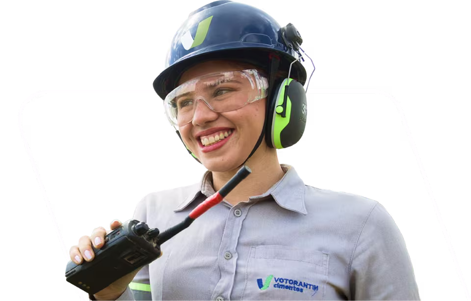 Jovem profissional sorrindo, com capacete, óculos de proteção e rádio comunicador
