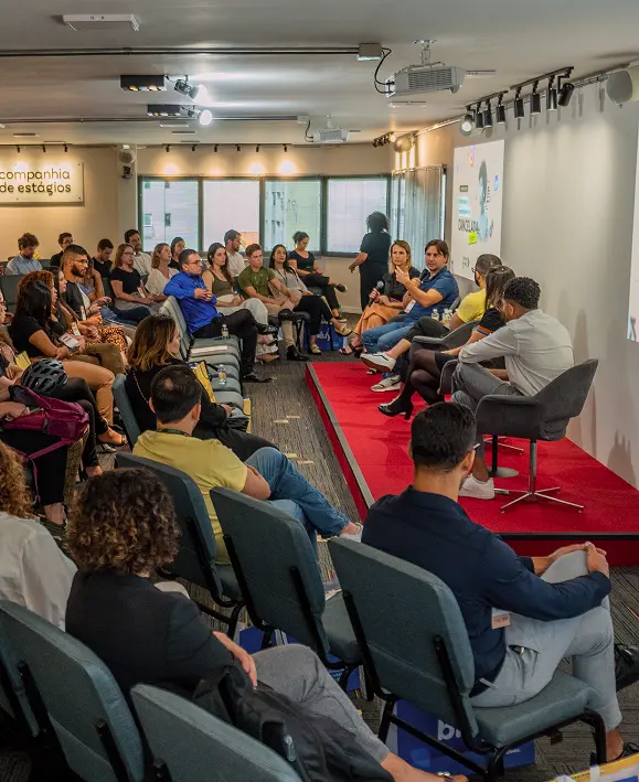 Painel de discussão no palco do auditório da Companhia de Estágios, com cinco convidados sentados e plateia assistindo