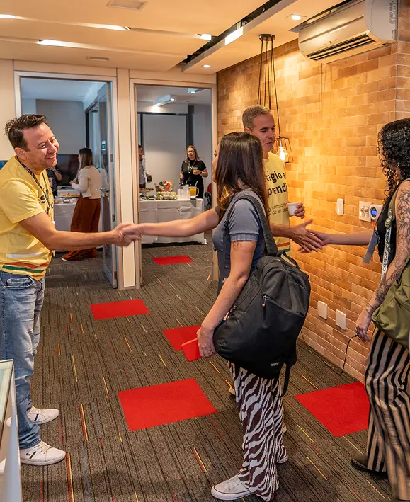 Pessoas se cumprimentam e sorriem durante recepção e networking na entrada do auditório