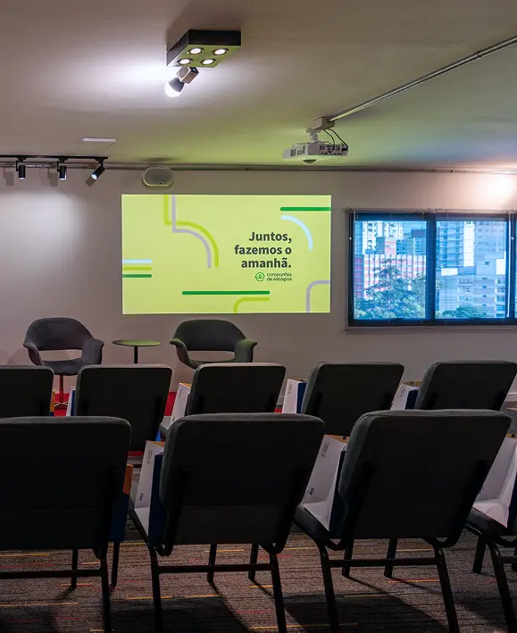 Palco do auditório da Companhia de Estágios com poltronas sobre tapete vermelho. No telão, a mensagem `Juntos, fazemos o amanhã`.